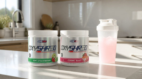 OxyShred Kiwi Strawberry and Cosmic Blast tubs on a kitchen bench beside a shaker of pink drink