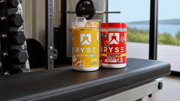 Ryse Loaded Pre Ring Pop Cherry and Loaded Pre Max Orange Cream tubs on a gym bench with a scoop on top