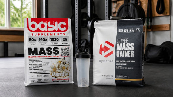 Basic Mass Gainer and Dymatize Super Mass Gainer tubs side by side on a garage gym floor with a shaker between them