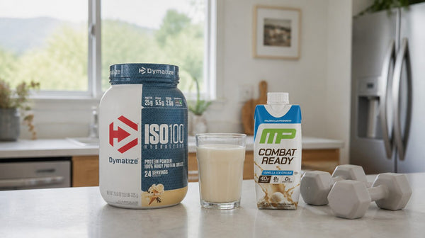 Dymatize ISO100 tub and a MusclePharm Combat Ready shake on a kitchen bench beside a glass of protein shake and light dumbbells