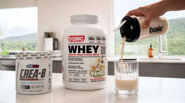 Shaker bottle being poured next to an EHPlabs Crea-8 creatine tub and a Basic Whey tub on a kitchen bench