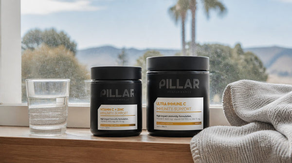 Pillar Performance Vitamin C + Zinc and Ultra Immune C on a kitchen windowsill with a glass of water