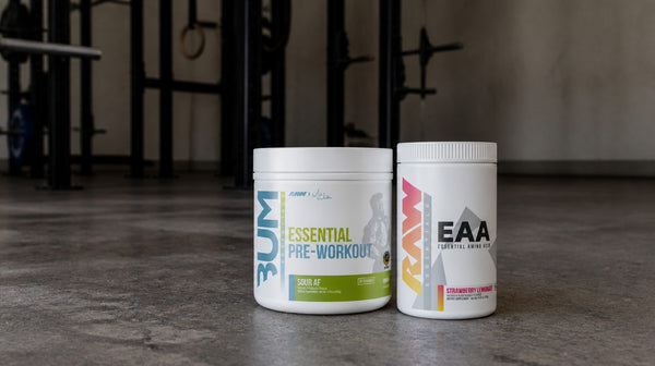 Raw Nutrition Essential pre-workout and Raw EAA tubs on a concrete gym floor with a squat rack behind
