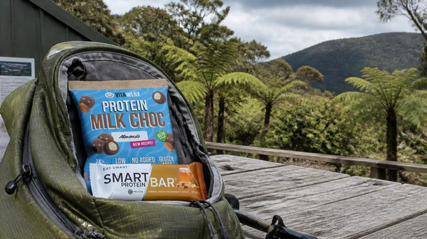 Protein bars, chocolate-coated almonds and energy gels laid out beside a tramping pack on a hut deck