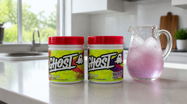 Two Ghost BCAA V2 tubs, Lemon Crush and Welch's Grape Cranberry, on a kitchen bench beside a jug of iced drink