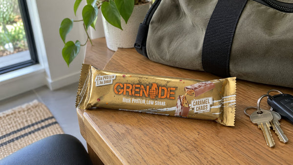 Grenade Caramel Chaos protein bar beside a gym bag on a desk