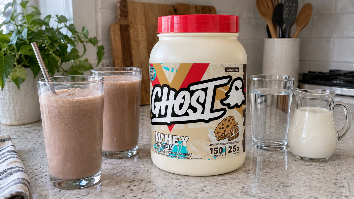 GHOST Whey Chocolate Chip Cookies beside two shakes, milk and water on a kitchen bench.
