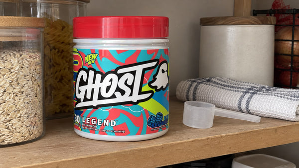 Closed GHOST Legend Blue Raspberry tub on a pantry shelf beside a dry scoop.