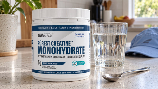 Athletech Purest Creatine Monohydrate beside water and a teaspoon on a kitchen bench.