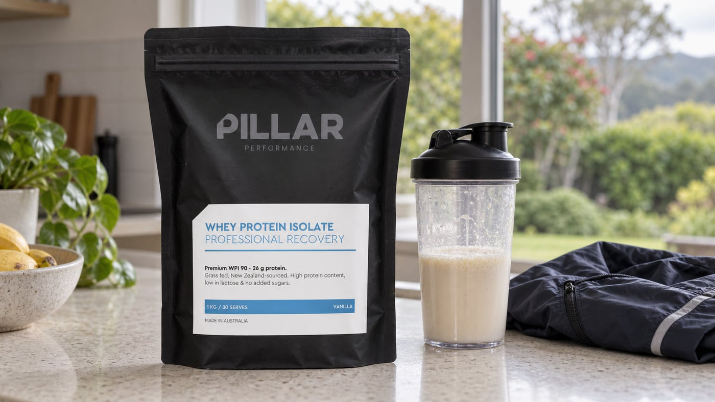 Pillar Performance Vanilla Whey Protein Isolate pouch beside a shaker on a kitchen island.