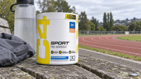 Cellucor C4 Sport Blue Raspberry tub and water bottle on a bench beside a running track.